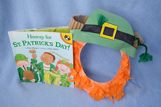 The book Hooray for St. Patricks day next to a mask decorated with a green hat, four-leaf clovers, and a red beard. 
