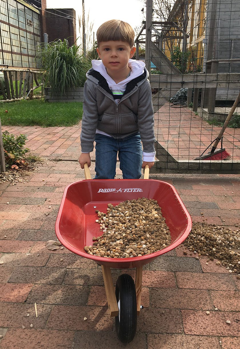Child holding red wheelbarrow filled with gravel in Our Backyard exhibit at LICM. 