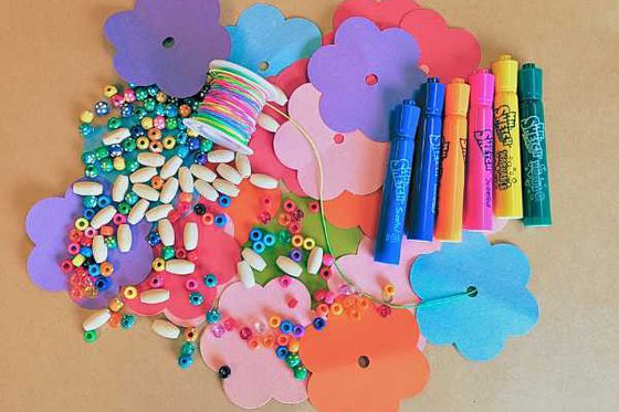 A pile of colorful paper flowers, beads, markers and a roll of multi-colored string. 