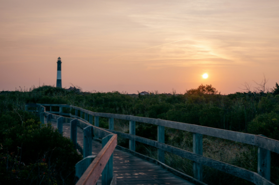 Scenic boardwalk to lighthouse at sunset on a coastal trail