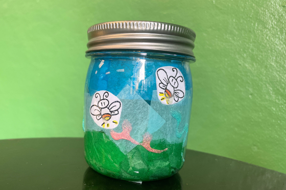 Glass mason jar decorated with colored tissue paper and paper lightning bugs. 