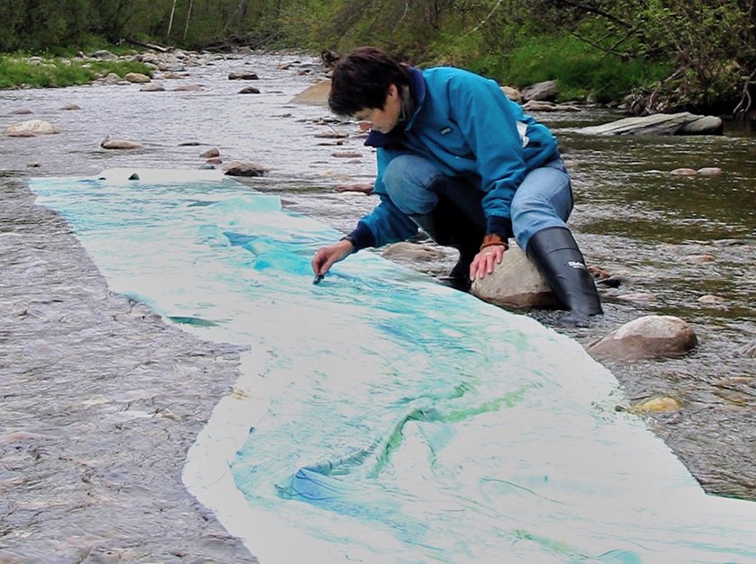 Image of woman paining on paper immersed in river.