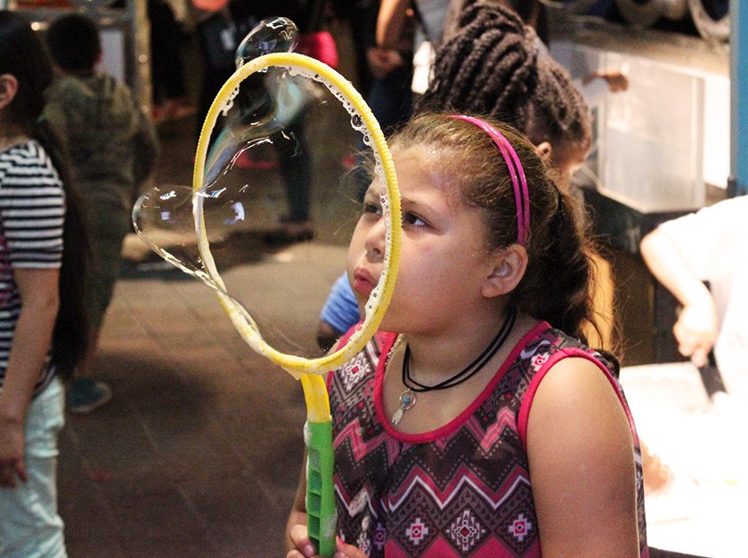 A girl blowing a bubble with a bubble wand. 