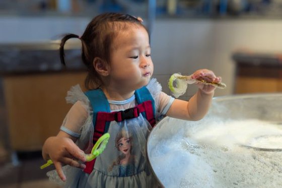Young girl uses a bubble wand made out of pipe cleaners to form different sized bubbles.