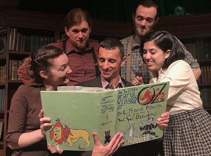 Five actors on stage reading The Wonderful Wizard of Oz book. 