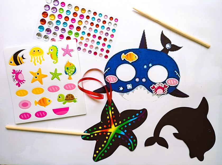 A variety of sea related crafts; a whale mask, sea stickers, a starfish and dolphin scratch pad, and colorful plastic jewels.