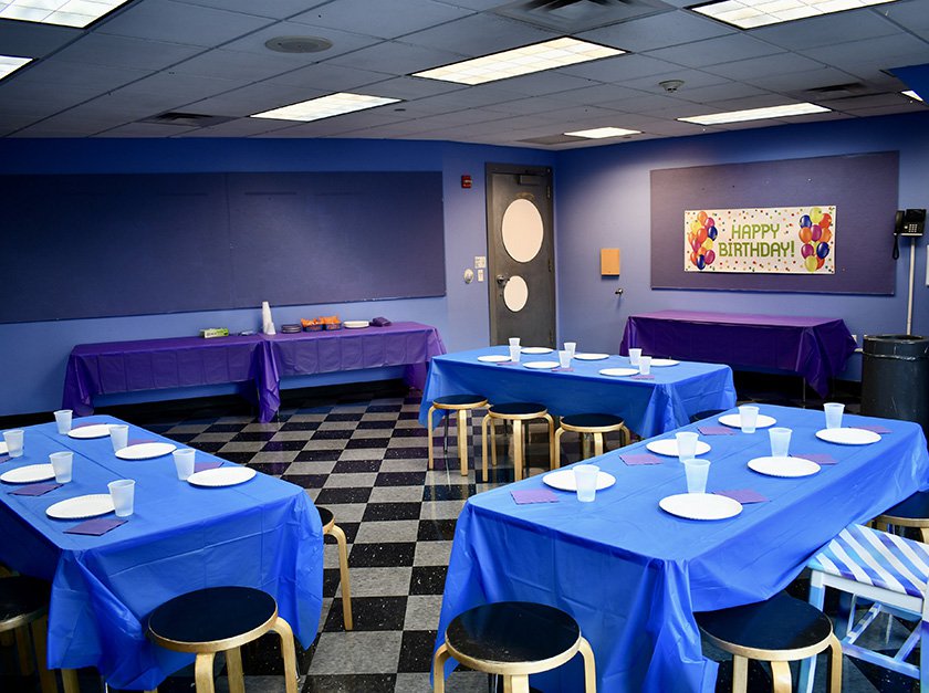 Museum studio with purple walls, six party tables set up and Happy Birthday banner on wall.