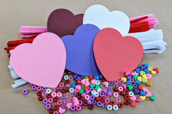 A pile of colorful round and heartshaped beads, paper hearts and pipe cleaners. 