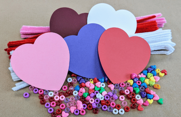 A pile of colorful round and heartshaped beads, paper hearts and pipe cleaners. 