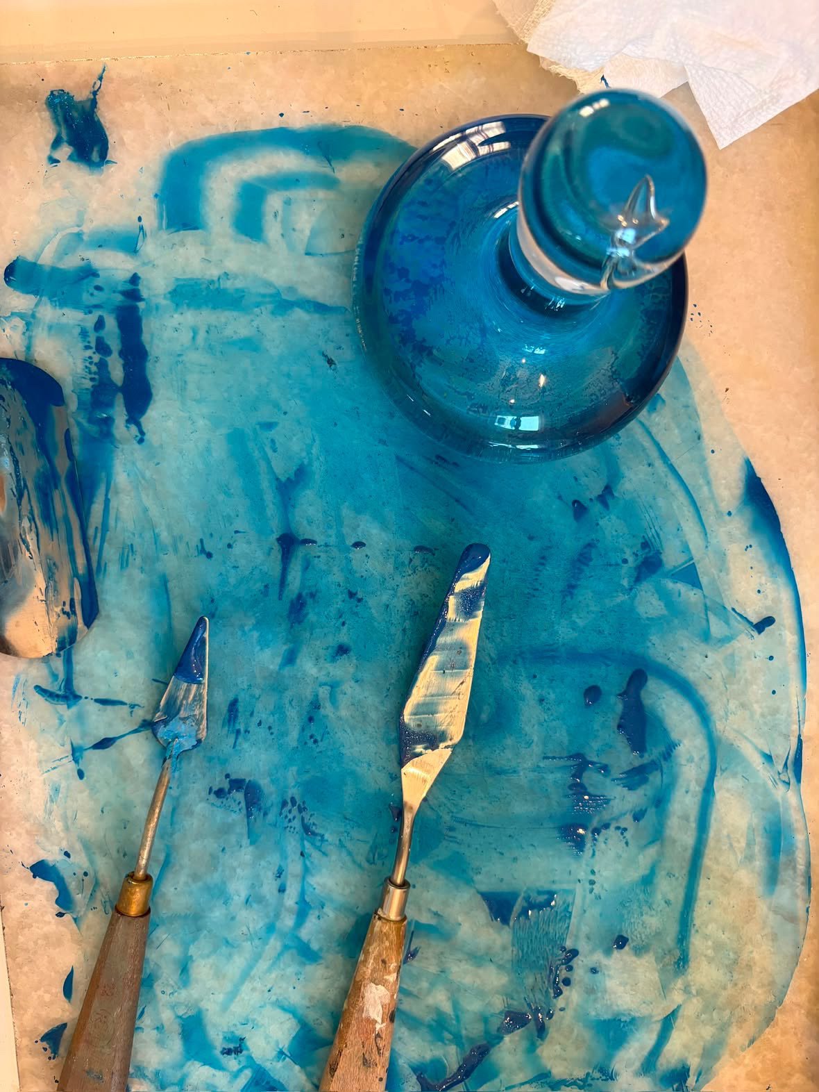 Blue watercolor paint on a cavnas with a glass mueller and two painting knives. 