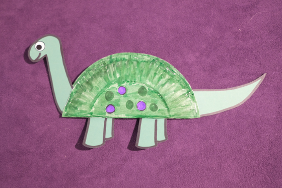 A green paper dinosaur with a body made of a paper plate cut in half, and glued together.