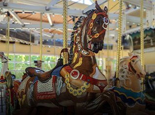 A close up of a dark brown carousel horese with other carousel horses in the background. 
