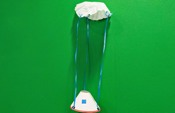 A paper shuttle attached to ribbon and a coffee filter as a parachute. 