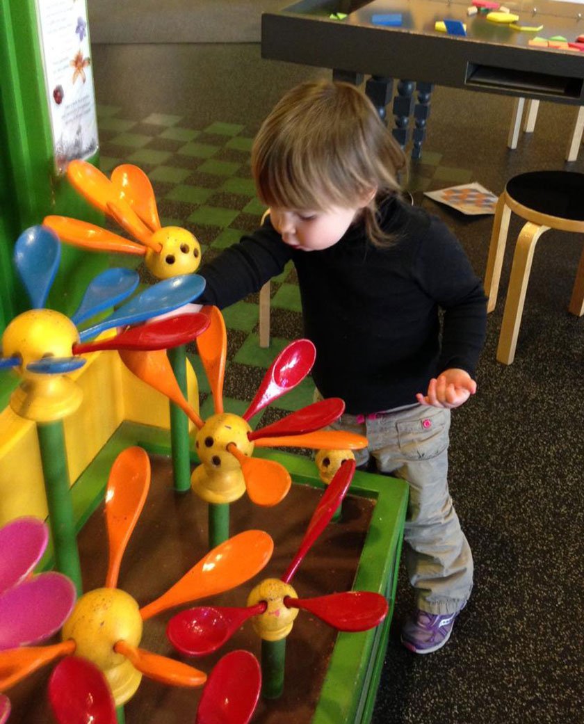 Child putting wooden spoon petals to create a flower in exhibit. 
