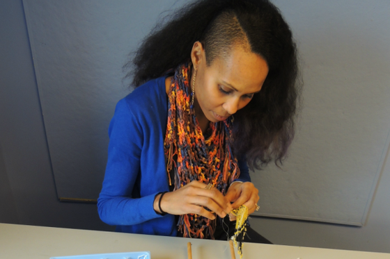 Artist creating a beaded necklace with yellow and black beads using a beading loom. 