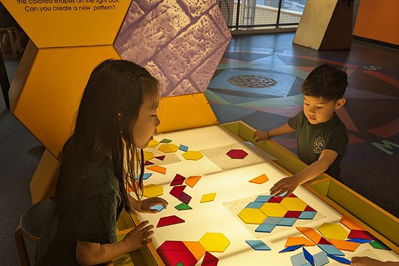 Two children standing at a light table playing with colorful shapes. 
