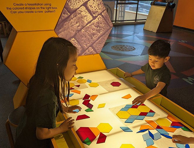 Two children standing at a light table playing with colorful shapes. 