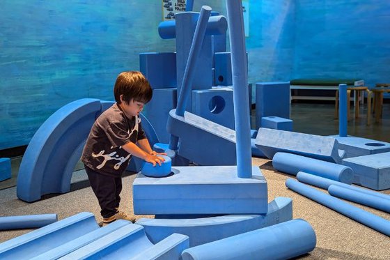 A child building a structure using large foam blue 'blocks'. 