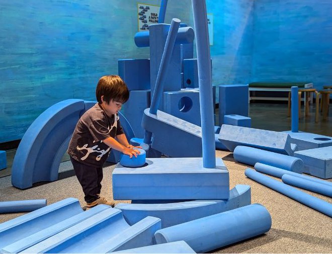 A child building a structure using large foam blue 'blocks'. 