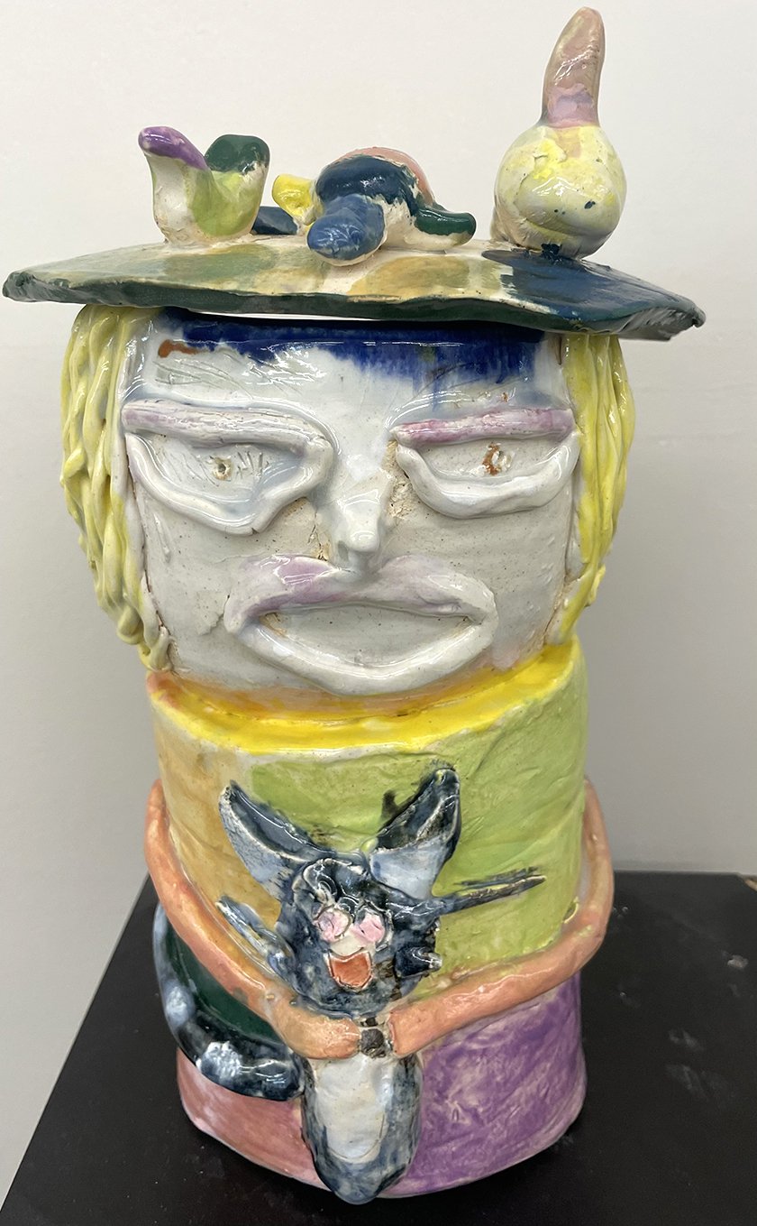 A ceramic sculpture of a girl holding a cat while balancing various objects on her head.