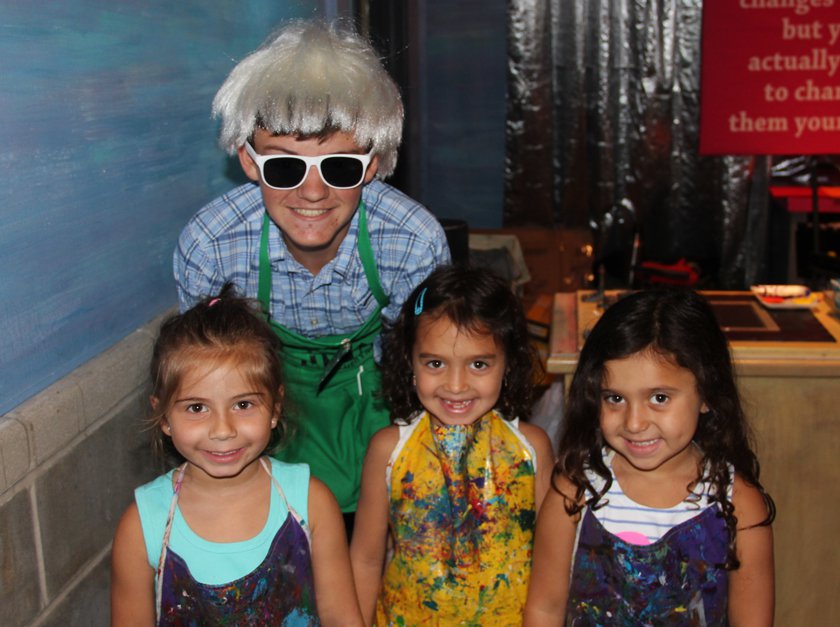 A Museum volunteer wearing a Andy Warhol wig standing with children. 