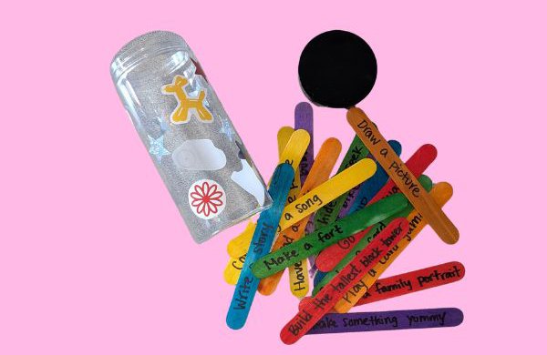 A plastic jar decorated with stickers and colorful popsicle sticks with prompts written on them. 