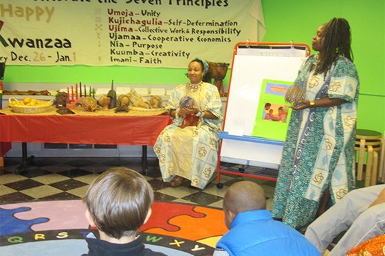 Two women in an LICM Studio teaching visitors about Kwanzaa dressed in traditional garb. 
