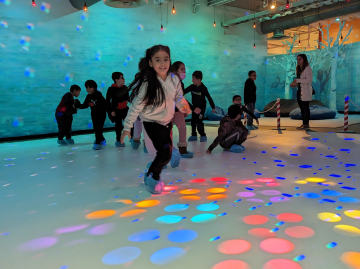 A group of children gliding on the plastic "ice" surrounded by colorful lights. 