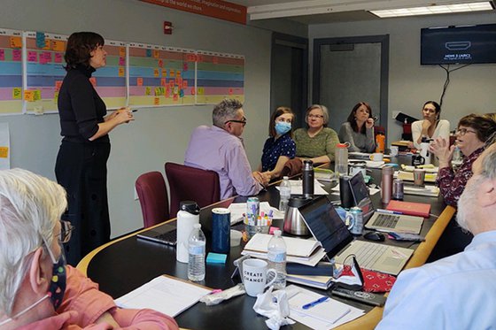 LICM staff sitting in a conference room while one staff member is standing in the middle of the room speaking. 