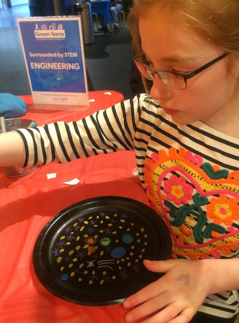 A young visitor creating a galaxy using metallic pens on a black paper plate. 