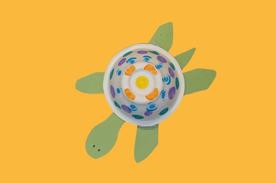 A paper sea turtle made with a paper bowl decorated with colorful dots as the shell and green paper legs, arms and head. 