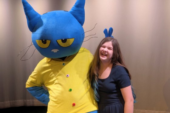 Pete the Cat character costume poses with teenage girl, making bunny ears behind her head.