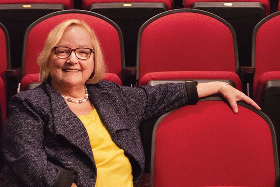 A smiling woman sitting in LICM's red theater seats while facing the camera with one arm across the seat next to her. 