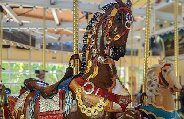 Close-up of a dark brown carousel horse decorated with bells and armor. 