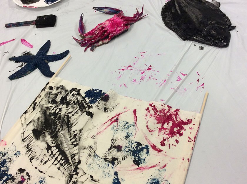 A piece of fabric painted by painting the back of a fish, crab, and starfish and placing it on the fabric. 