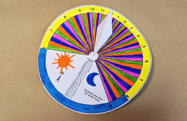 A colorful paper sundial featuring a drawing of a sun and moon. 