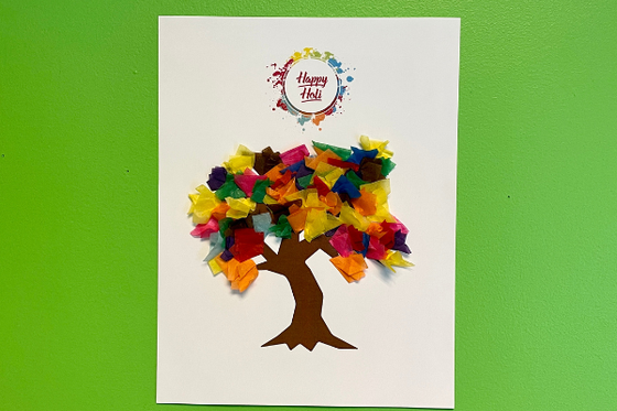 A paper tree with a brown trunk and multi-colored tissue paper as leaves with rainbow text "Happy Holi" above. 