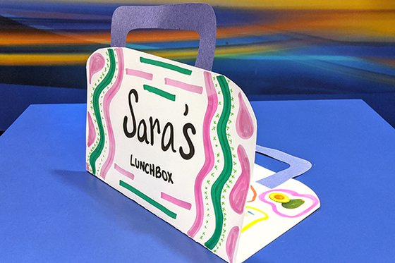 A white, paper lunch box decorated with pink and green lines. 