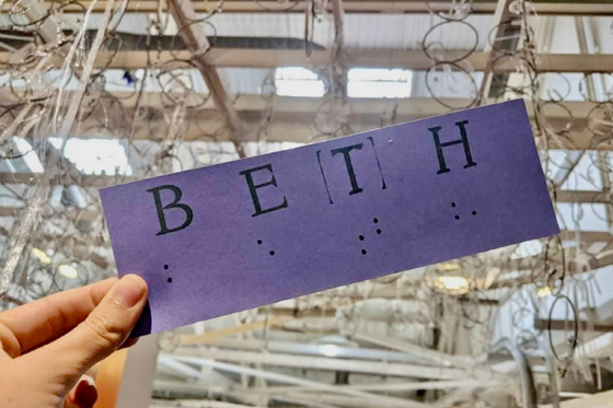 A piece of card stock with the name BETH written in ink, and in braille below it. 