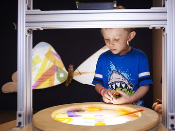 A child looking into a light box with a glowing butterfly in the background. 