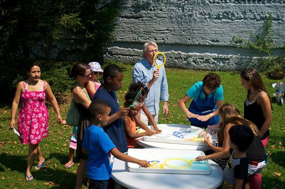 Children and adults outside using large bubble wands to blow bubbles.