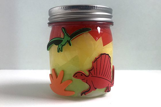A small yellow glass jar with various soft dinosaur stickers. 