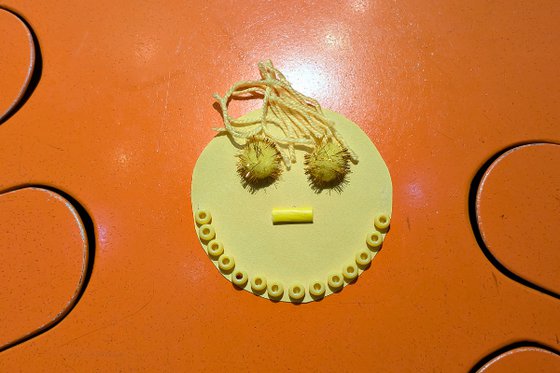 A yellow paper sun decorated with mixed media; yarn, pompoms, and beads. 