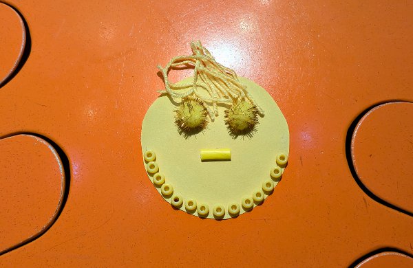 A yellow paper sun decorated with mixed media; yarn, pompoms, and beads. 