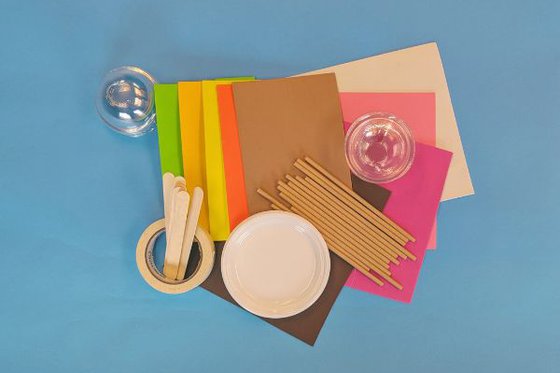Multicolored foam paper, plastic plates, popsicle sticks and plastic tops against a blue background. 