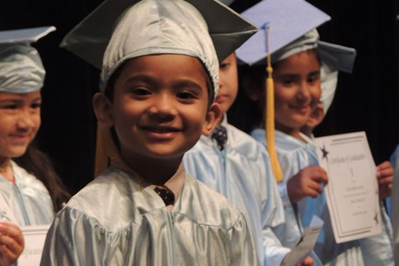 Pre-K program graduate in cap and gown on stage. 
