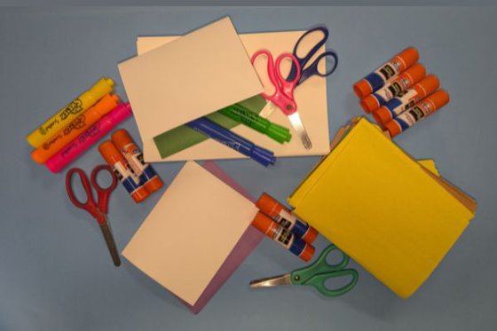 A scattered pile of colored coonstruction paper, markers, scissors and glue sticks. 