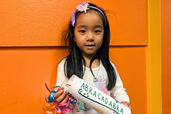A child looking at the camera while holding a white handmade confetti popper. 