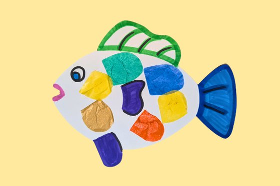 A paper colorful fish decorated with tissue paper scales on a yellow background.