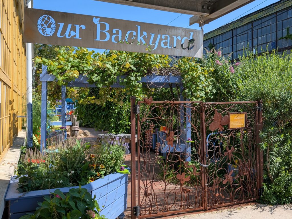The gate leading into Our Backyard with a view of flowers.